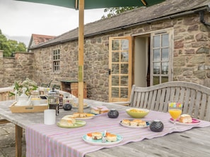 Un bâtiment rustique en pierre, avec une table en bois dressée pour un repas, où l’on peut voir différents plats et une boisson.