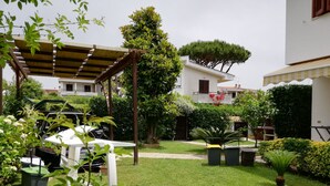 A well-maintained garden with a pergola, white lounge chairs, and various potted plants. - VILLA Mattia & Luca (Lido di Cincinnato - Anzio) (Anzio)