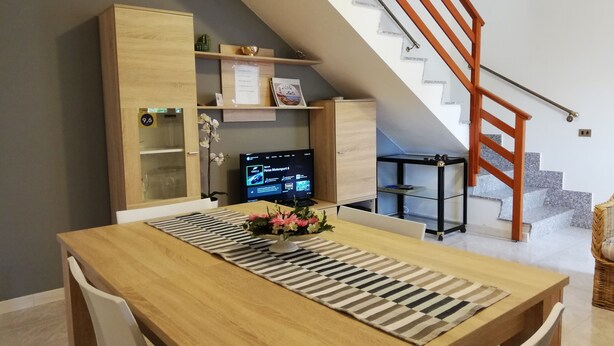 A dining area with a wooden table, chairs, a TV, and a staircase with a wooden railing. - VILLA Mattia & Luca (Lido di Cincinnato - Anzio) (Anzio)