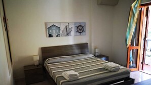 A bedroom with a bed, two bedside tables, a wall-mounted artwork, and a window with a curtain. - VILLA Mattia & Luca (Lido di Cincinnato - Anzio) (Anzio)