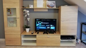 A wooden entertainment unit with a flat-screen TV, gaming console, and remote controls. - VILLA Mattia & Luca (Lido di Cincinnato - Anzio) (Anzio)