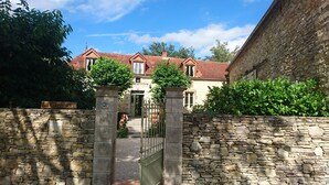 Ein Gebäude mit Steinmauern, einem traditionellen roten Ziegeldach, einem verschlossenen Eingang und üppiger Bepflanzung.