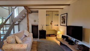 Ein Wohnzimmer mit Treppe, einer Couch, einem Fernseher und einem Kamin.