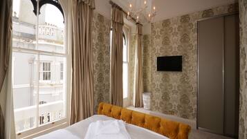 A hotel room with a large bed, a chandelier, a wardrobe, and a view of a building outside.