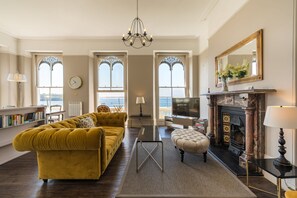 Un salón amplio con un sofá amarillo, una chimenea y grandes ventanales con vistas.