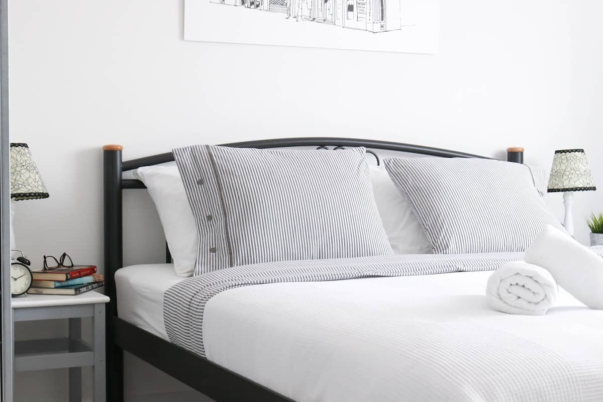A neatly made bed with striped bedding, a bedside table with a lamp, and a framed picture on the wall.