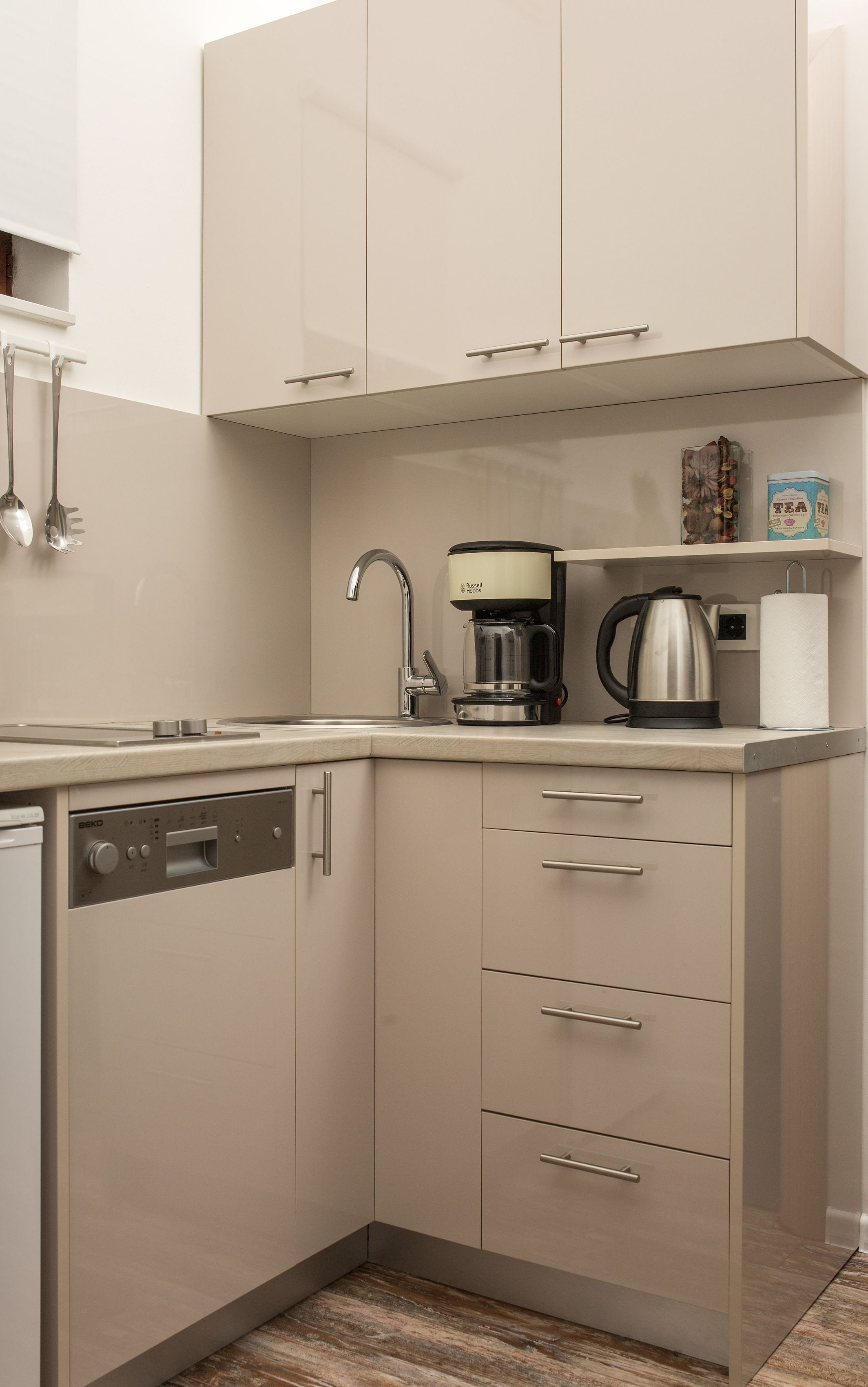 Cocina compacta con lavavajillas, cafetera y hervidor sobre la encimera.