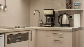Cocina compacta con lavavajillas, cafetera y hervidor sobre la encimera.