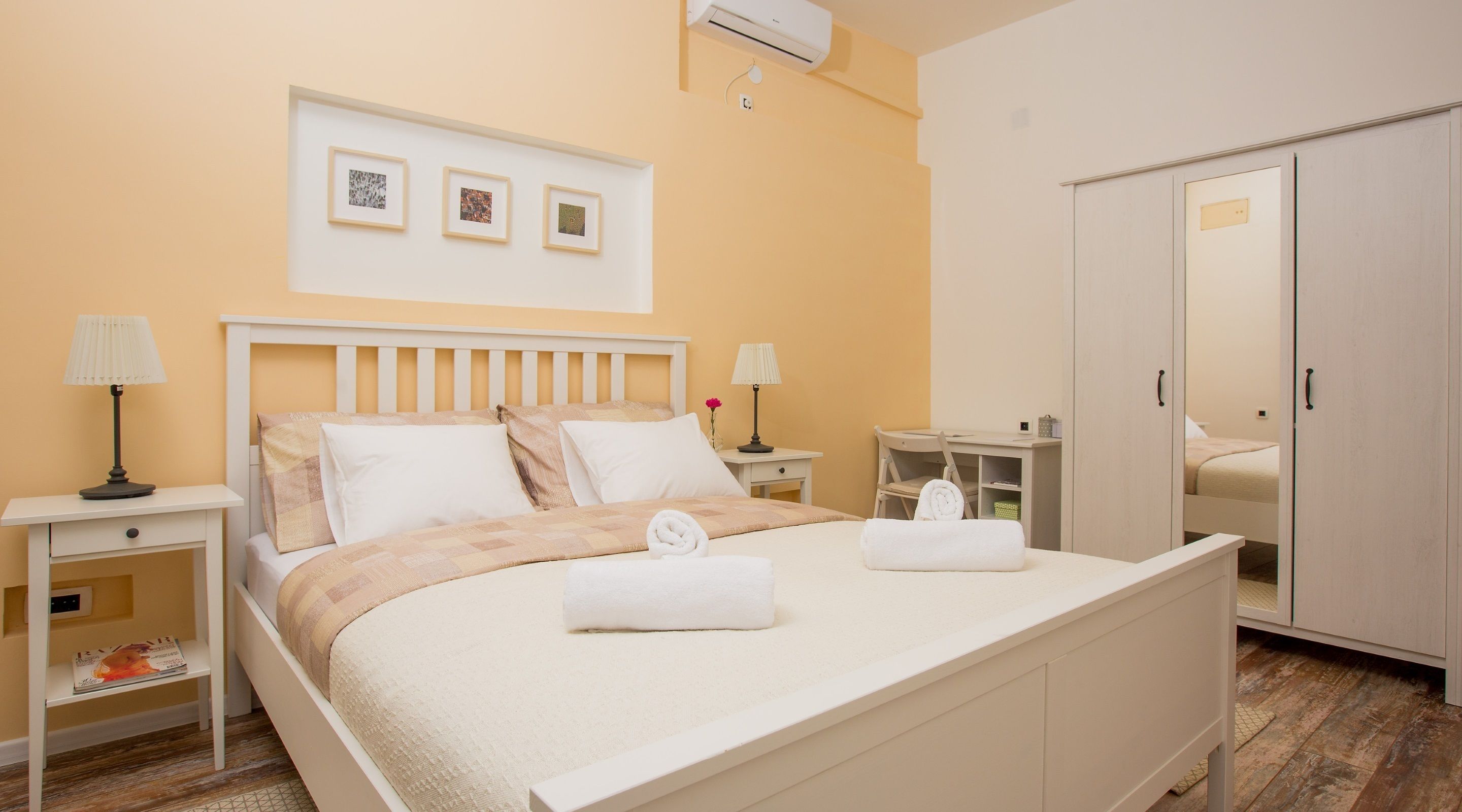 A neatly arranged bedroom with a bed, bedside tables, a desk, and a wardrobe.