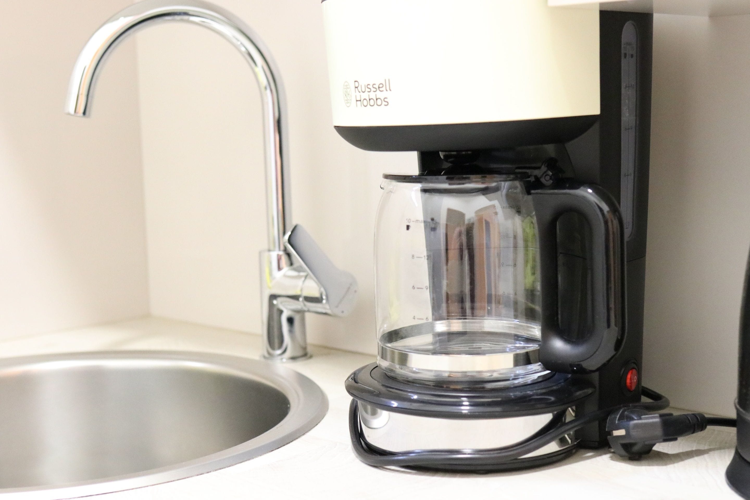 Een keuken met een moderne koffiezetapparaat, een roestvrijstalen spoelbak en een glazen kan.