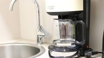 Een keuken met een moderne koffiezetapparaat, een roestvrijstalen spoelbak en een glazen kan.