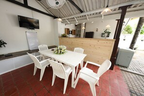 Un espace repas comprenant une table et des chaises blanches, un comptoir en bois et un téléviseur fixé au mur.
