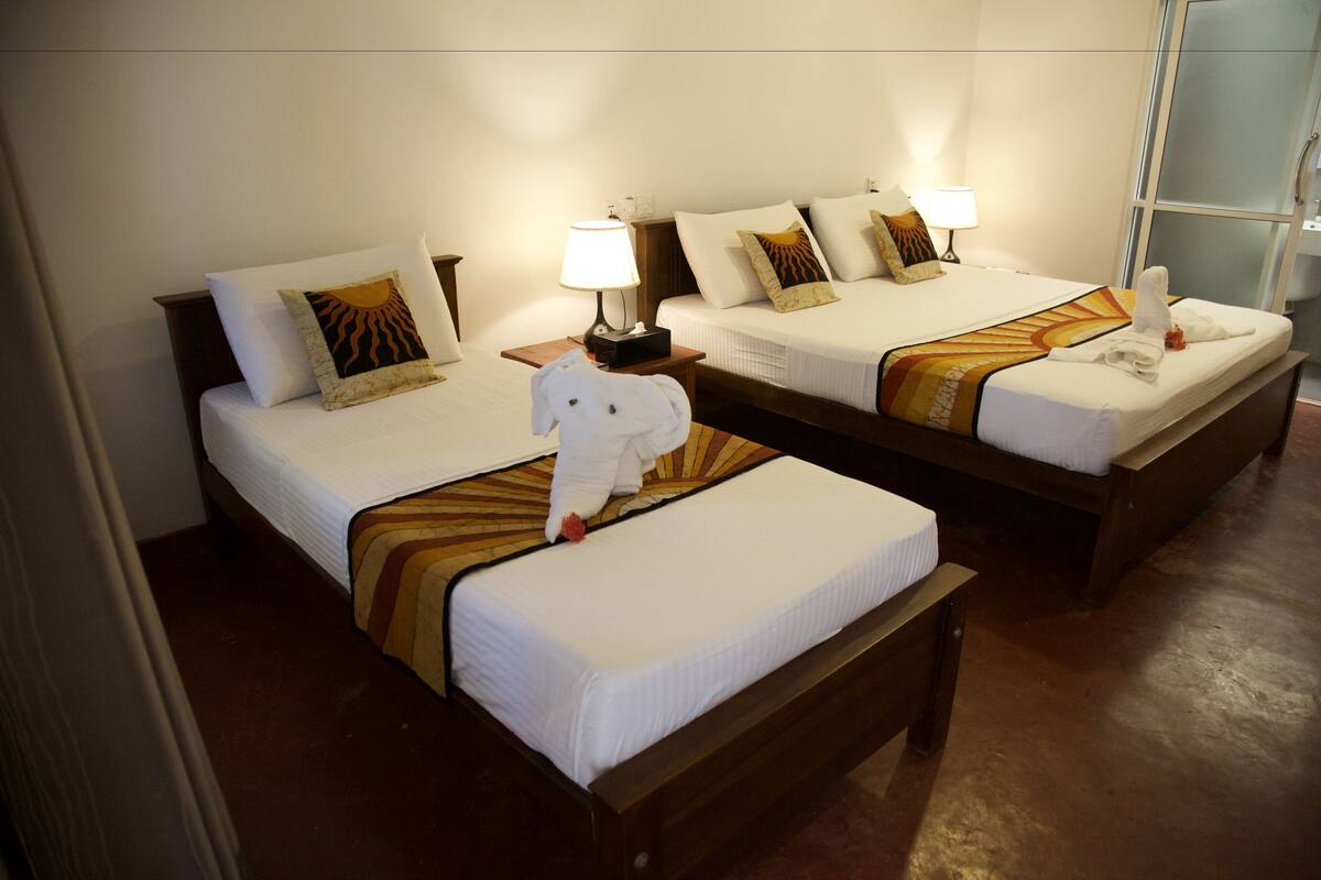 A hotel room with two beds, each with a white comforter, pillows, and a bedside lamp.