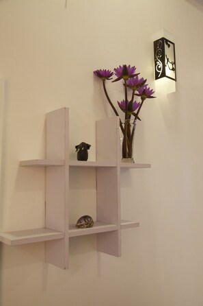 Un mur épuré agrémenté de deux étagères murales, dont l’une supporte un vase décoratif orné de fleurs violettes et d’une petite figurine, et l’autre, une coquille.