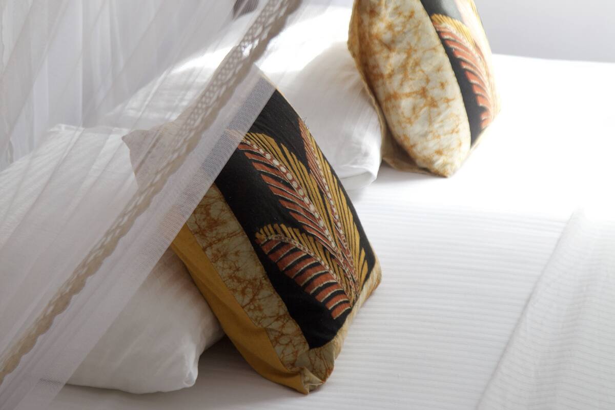 A bed with white linens and decorative pillows with a leaf pattern.