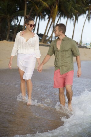 Un couple se promène sur une plage, avec des palmiers en arrière-plan.