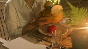 A person seated at a table with a plate of food, a glass, and a candle.