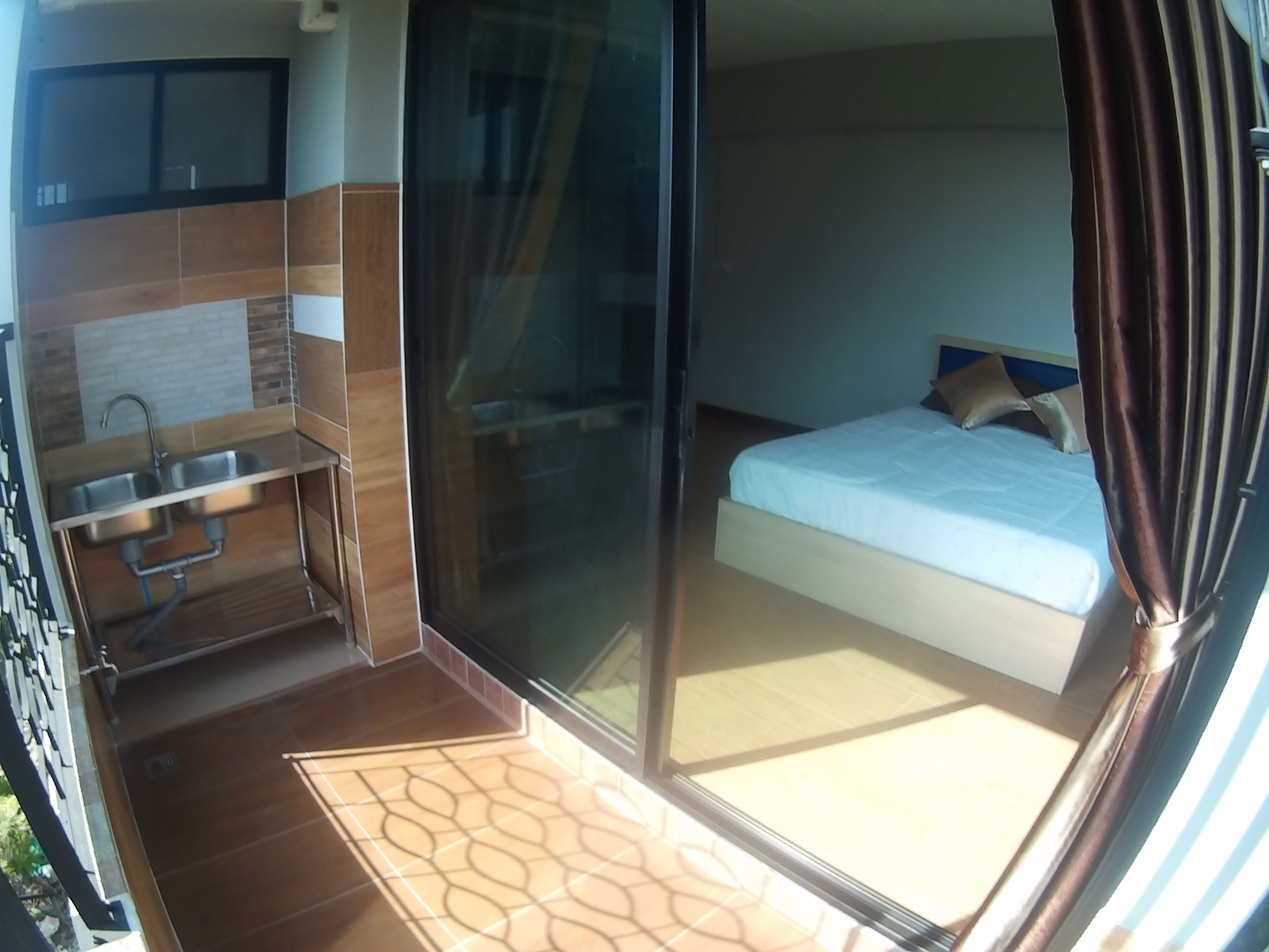 A compact room with a bed, a small kitchenette, and a sliding glass door leading to a balcony.