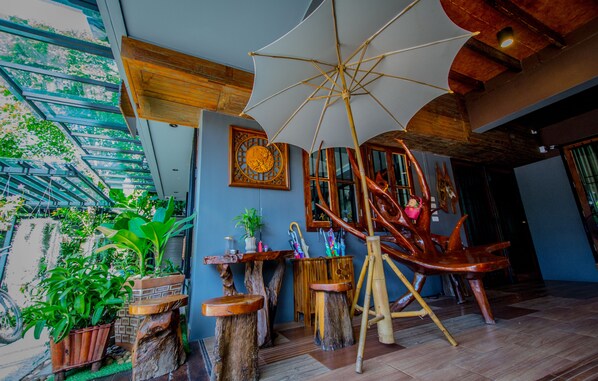 A room with a large umbrella, wooden furniture, and potted plants.