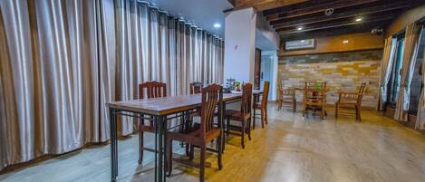 Un comedor con una mesa larga y sillas, suelo de madera y pared de piedra.