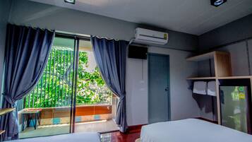 A hotel room with two beds, a balcony with curtains, an air conditioning unit, a door, and a small table.