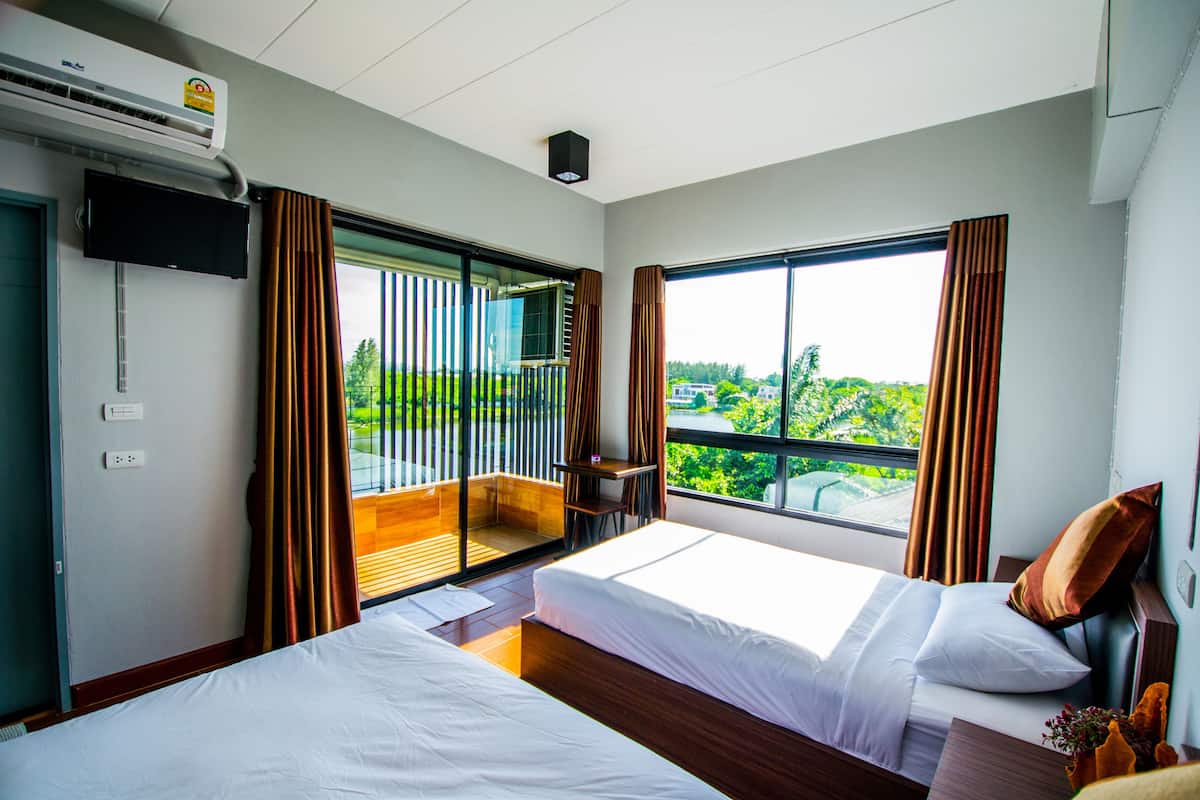 A hotel room with two beds, a TV, a balcony with a view, and an air conditioning unit.