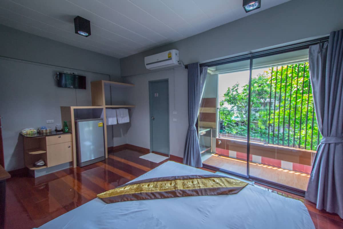 A hotel room with a bed, a wardrobe, a desk, a television, and a balcony with curtains.