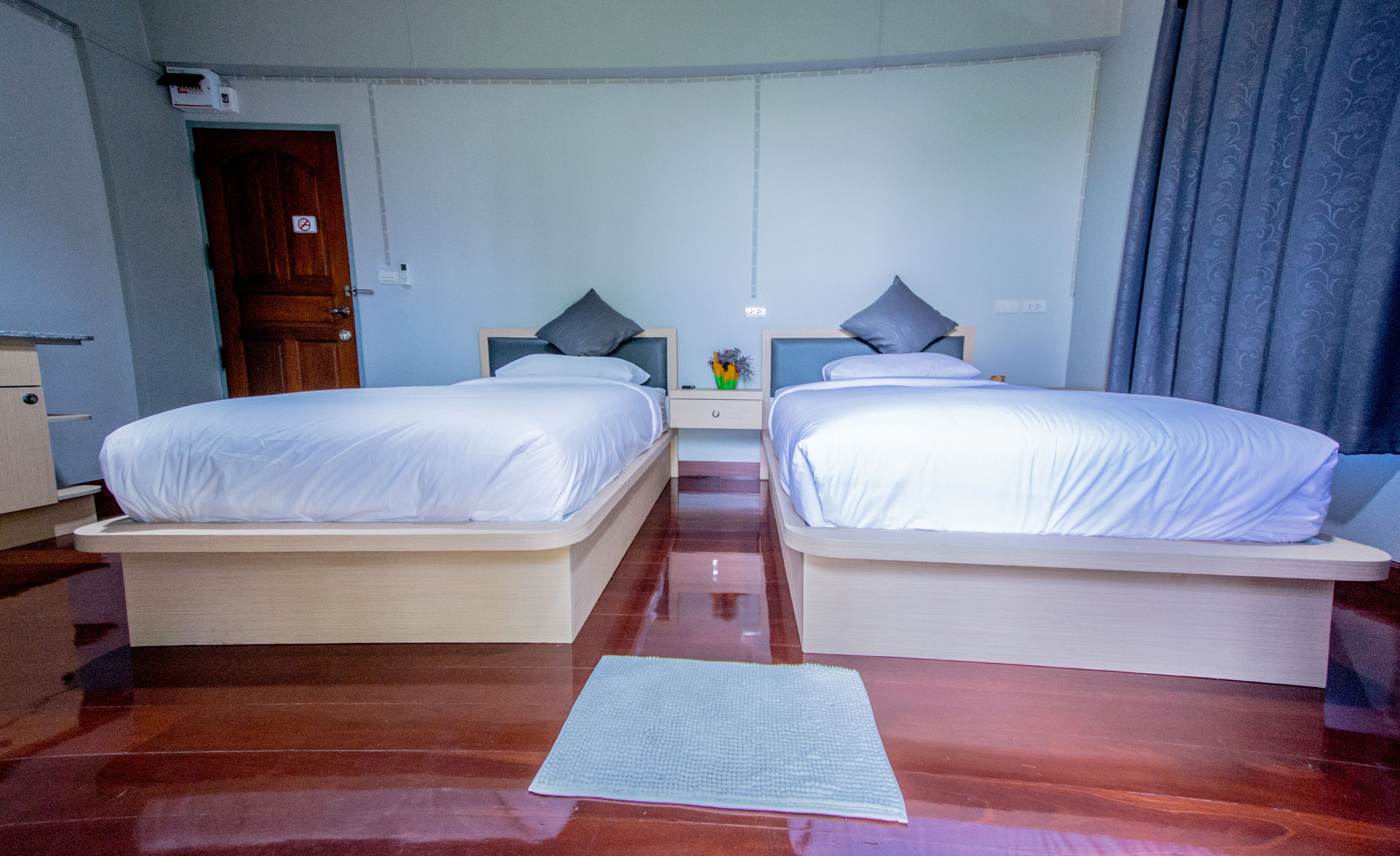 Habitación de hotel con dos camas, piso de madera, una mesita con un florero y una puerta.