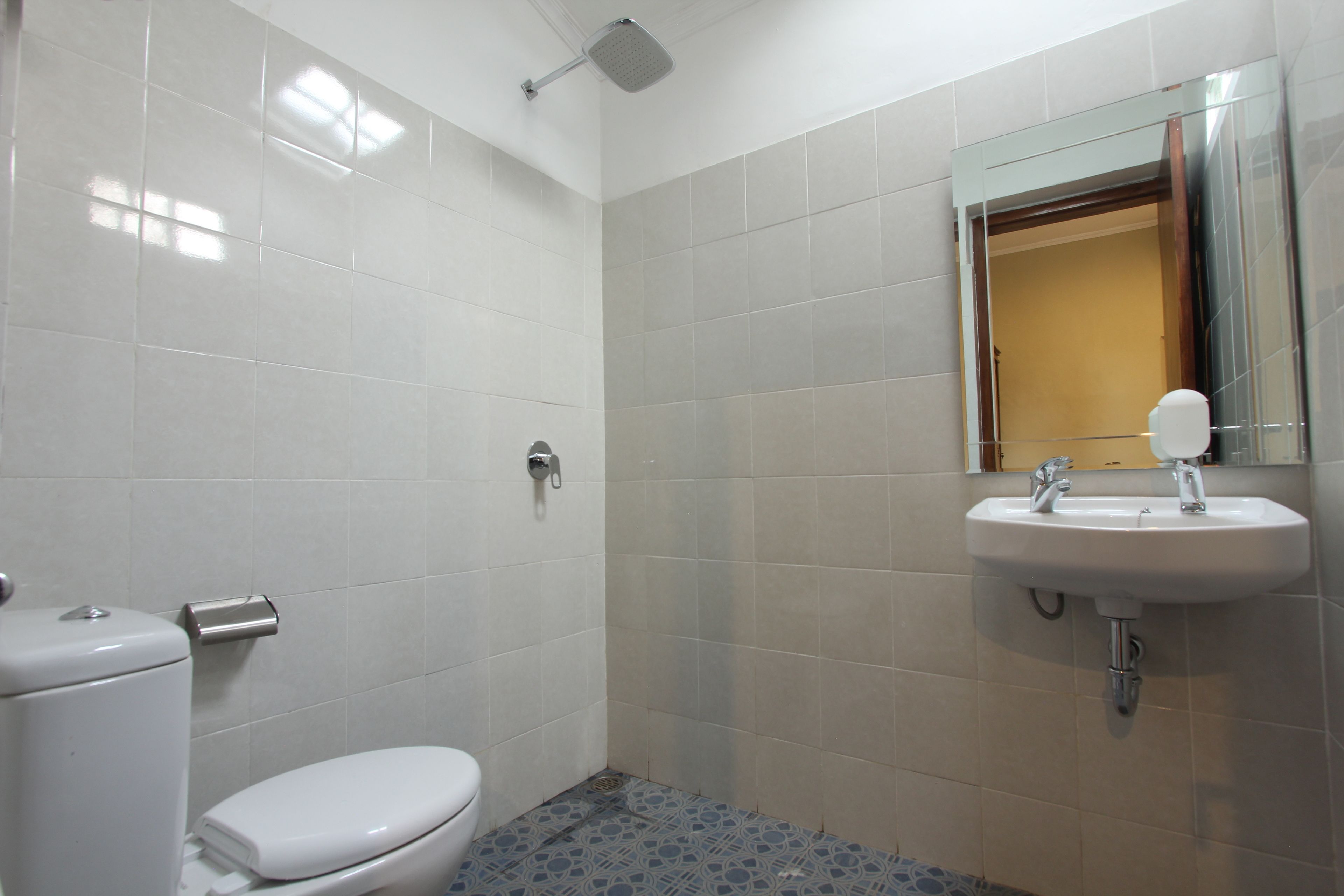 Ein Badezimmer mit weißen Fliesen, einer Toilette, einem Waschbecken und einer Dusche.