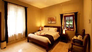 A bedroom with a bed, bedside tables, a chair, a window, and a painting on the wall. - Griya Gendhis Saraswati (Klaten)