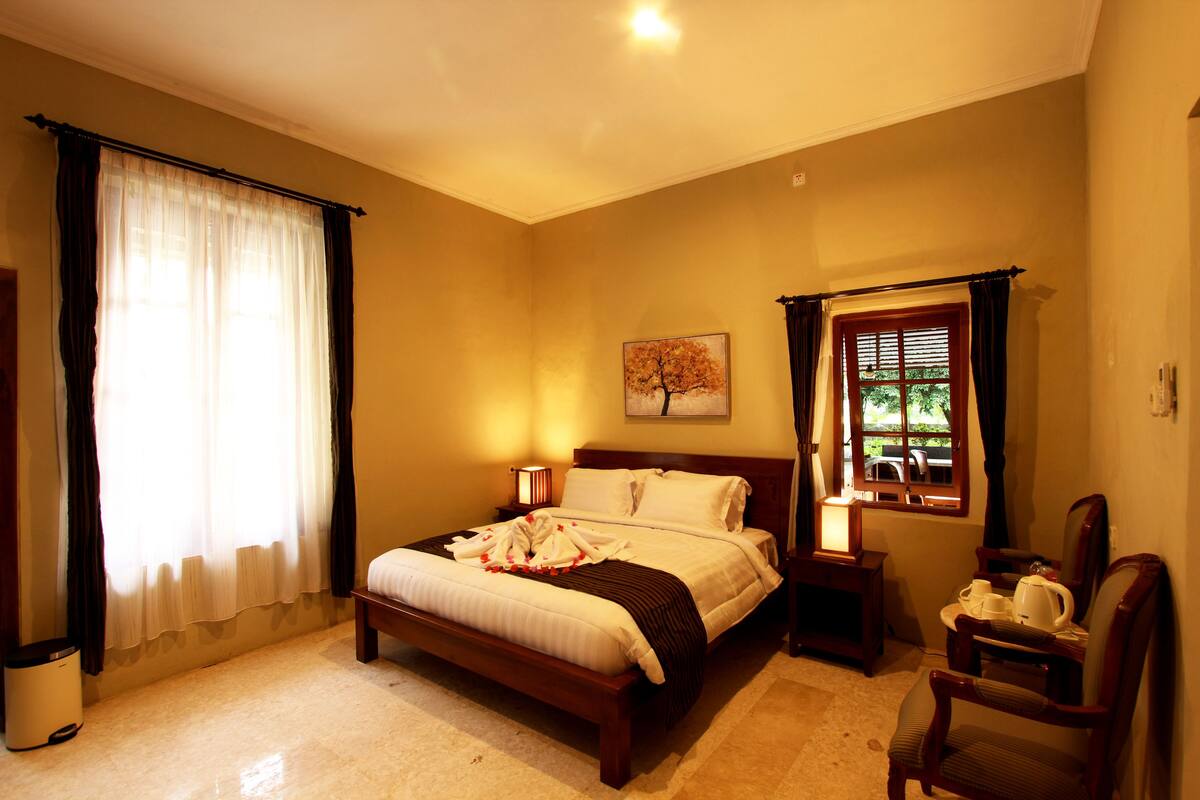 Une chambre à coucher avec un lit, des tables de chevet, une chaise, une fenêtre et un tableau au mur.