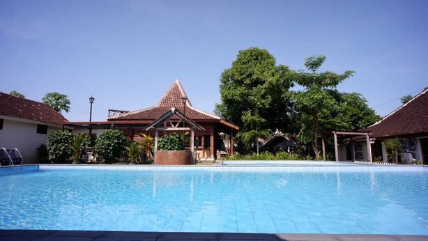 A swimming pool with a gazebo, surrounded by buildings with tiled roofs and greenery. - Griya Gendhis Saraswati (Klaten)