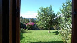 A view through an open door into a well-maintained garden with a grassy lawn, a tree, and a stone wall.