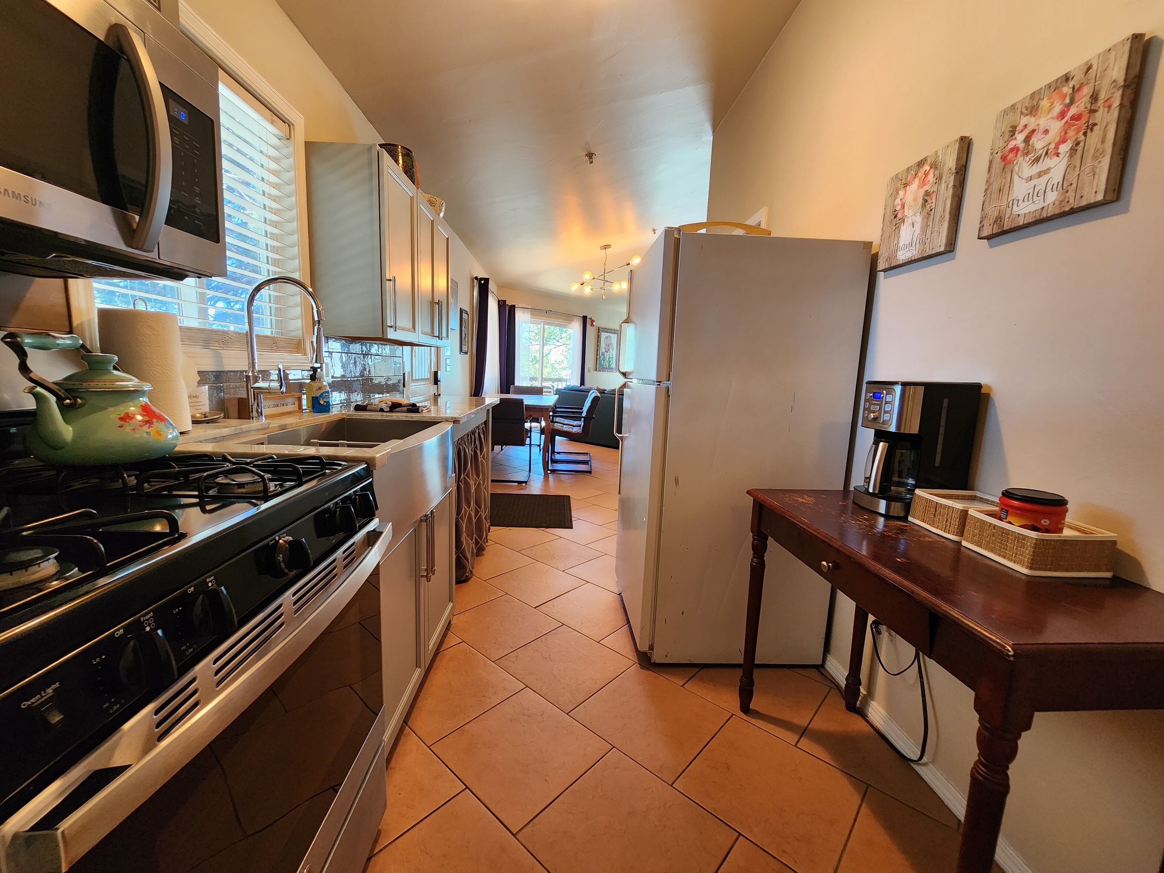 Eine kompakte Küche mit Mikrowelle, Herd, Spüle und Kühlschrank. Im Hintergrund ist eine Essecke mit Tisch und Stühlen zu sehen.