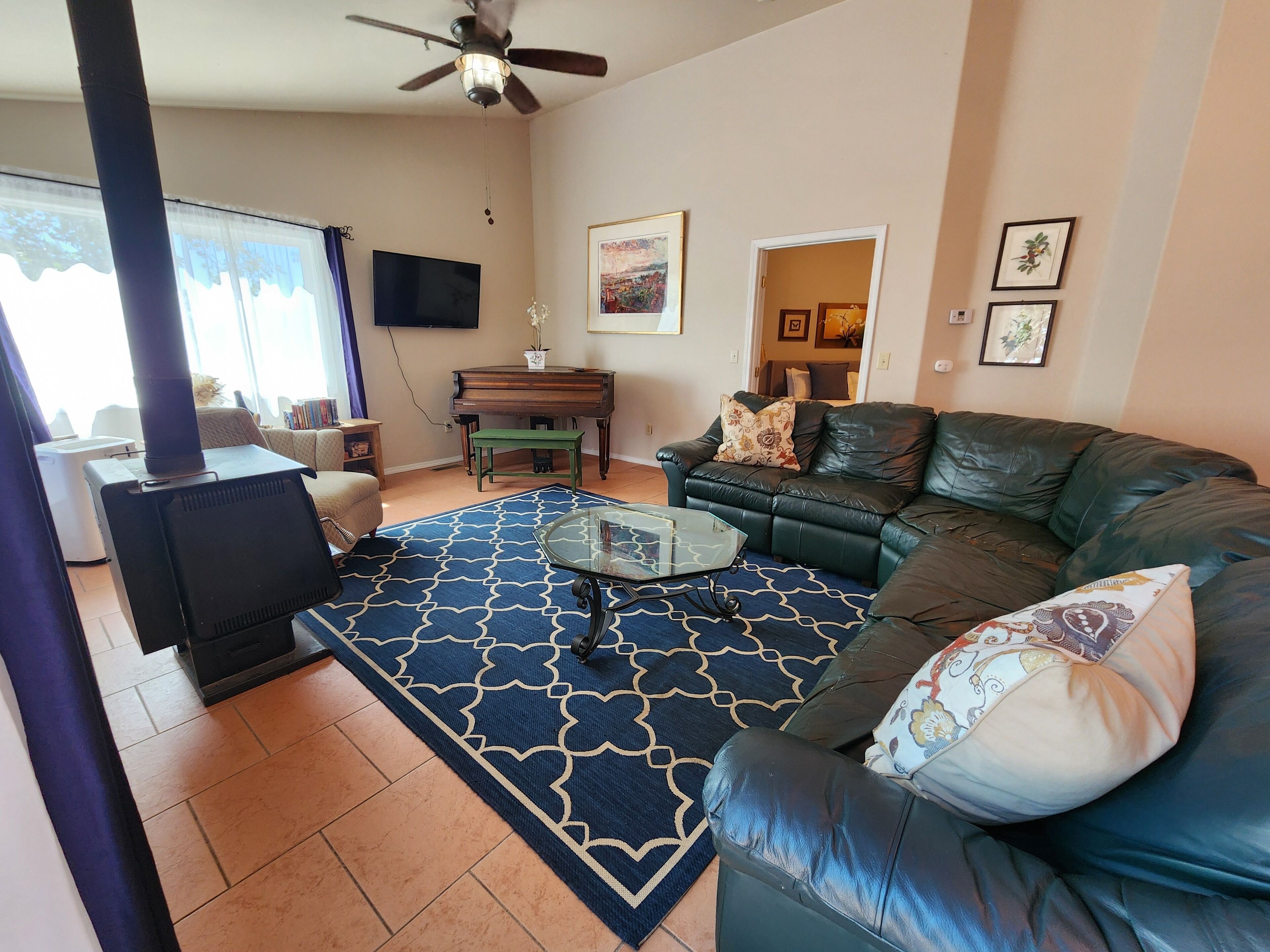 Una sala de estar con sofá, una mesa de centro de vidrio, chimenea, televisor y piano.