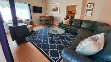 Una sala de estar con sofá, una mesa de centro de vidrio, chimenea, televisor y piano.