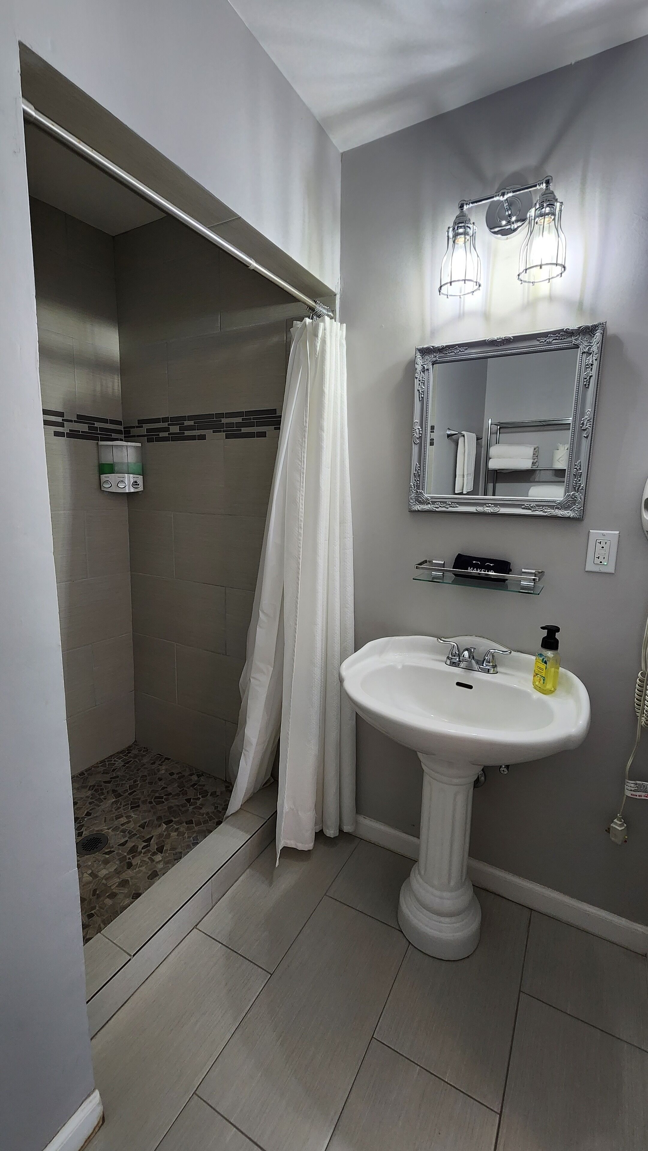 A bathroom with a shower, a sink, a mirror, and a light fixture.