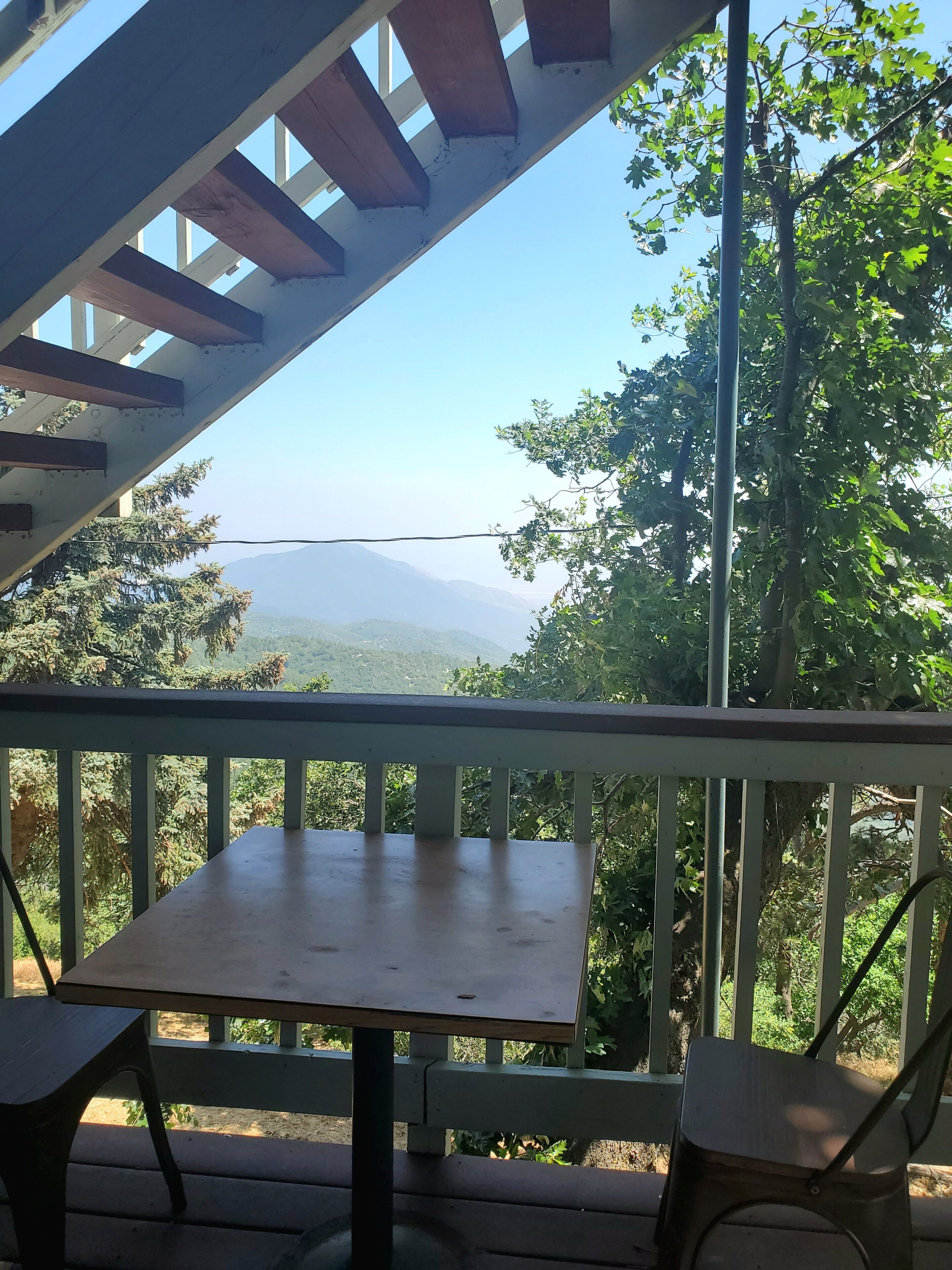 A wooden table and chairs on a balcony with a view of a mountain range and trees.