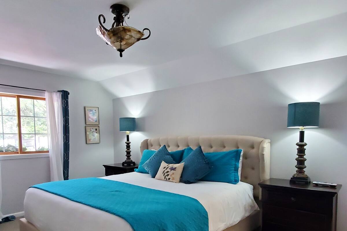 A bedroom with a large bed, two bedside tables, a window with curtains, and a ceiling light fixture.