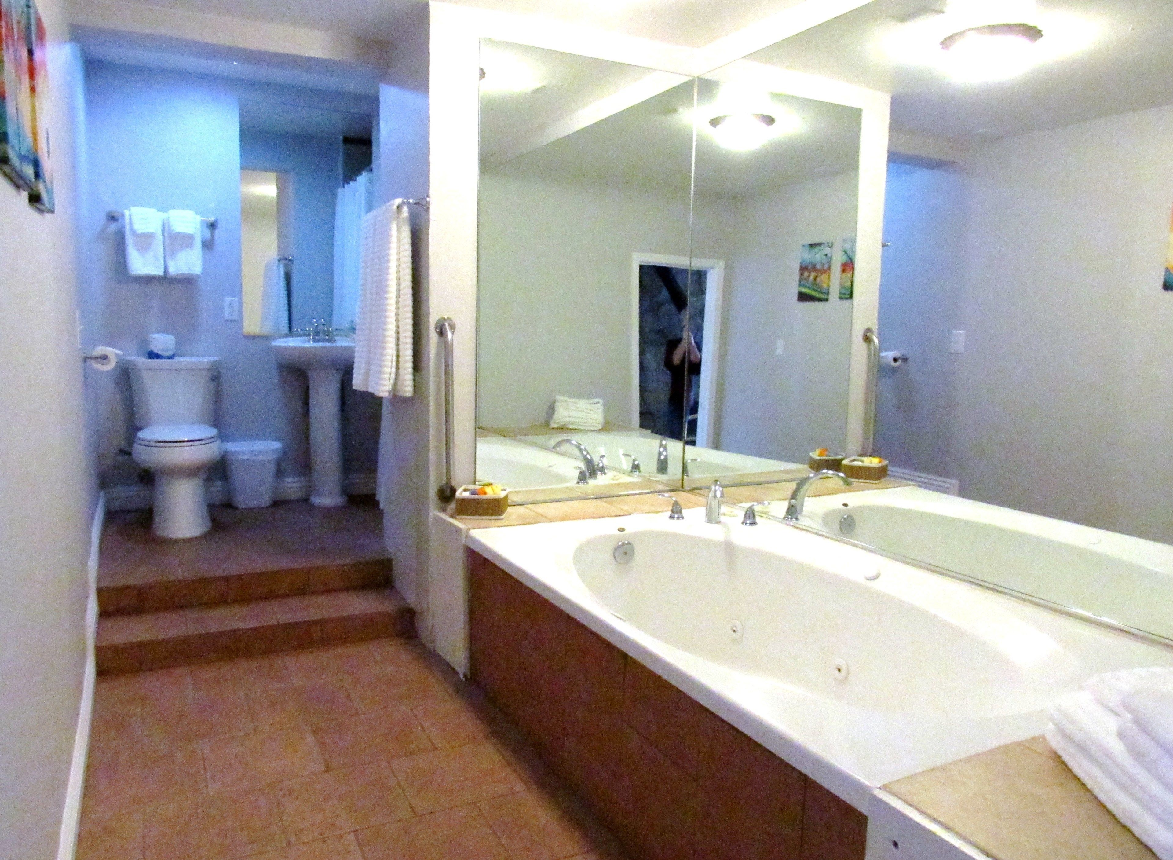 A bathroom with a large bathtub, a sink, and a toilet. There is a mirror above the sink and a towel rack on the wall.