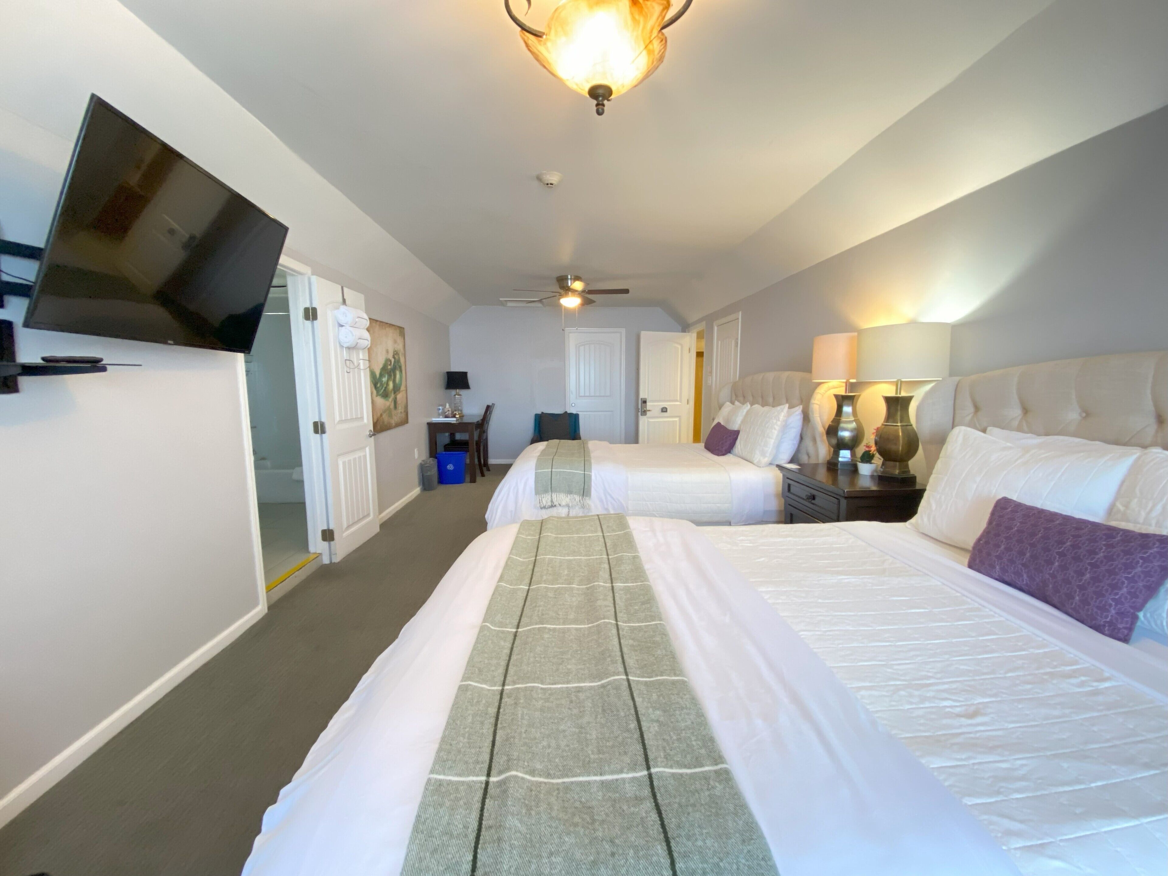 A hotel room with two beds, a TV, a desk, and a ceiling fan.