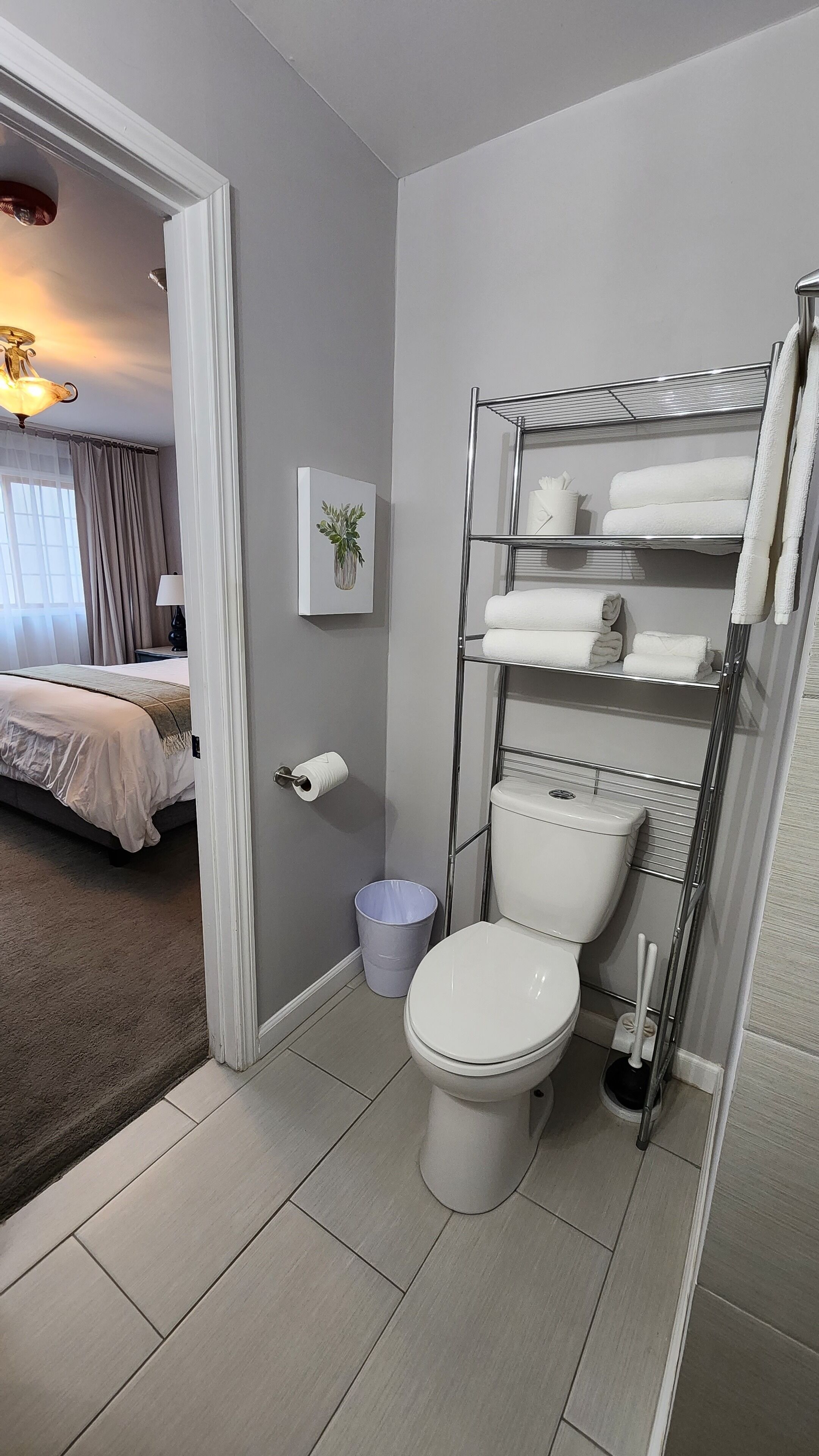 A bathroom with a toilet, a shelf with towels, a trash bin, and a toilet paper holder.