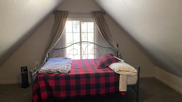 Una cama individual en una habitación con techo inclinado, una ventana con cortinas y un radiador en la pared.