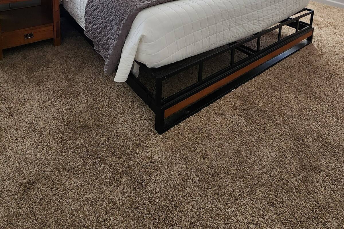 A bedroom with a bed, two bedside tables, a lamp, a painting, and a ceiling light fixture.