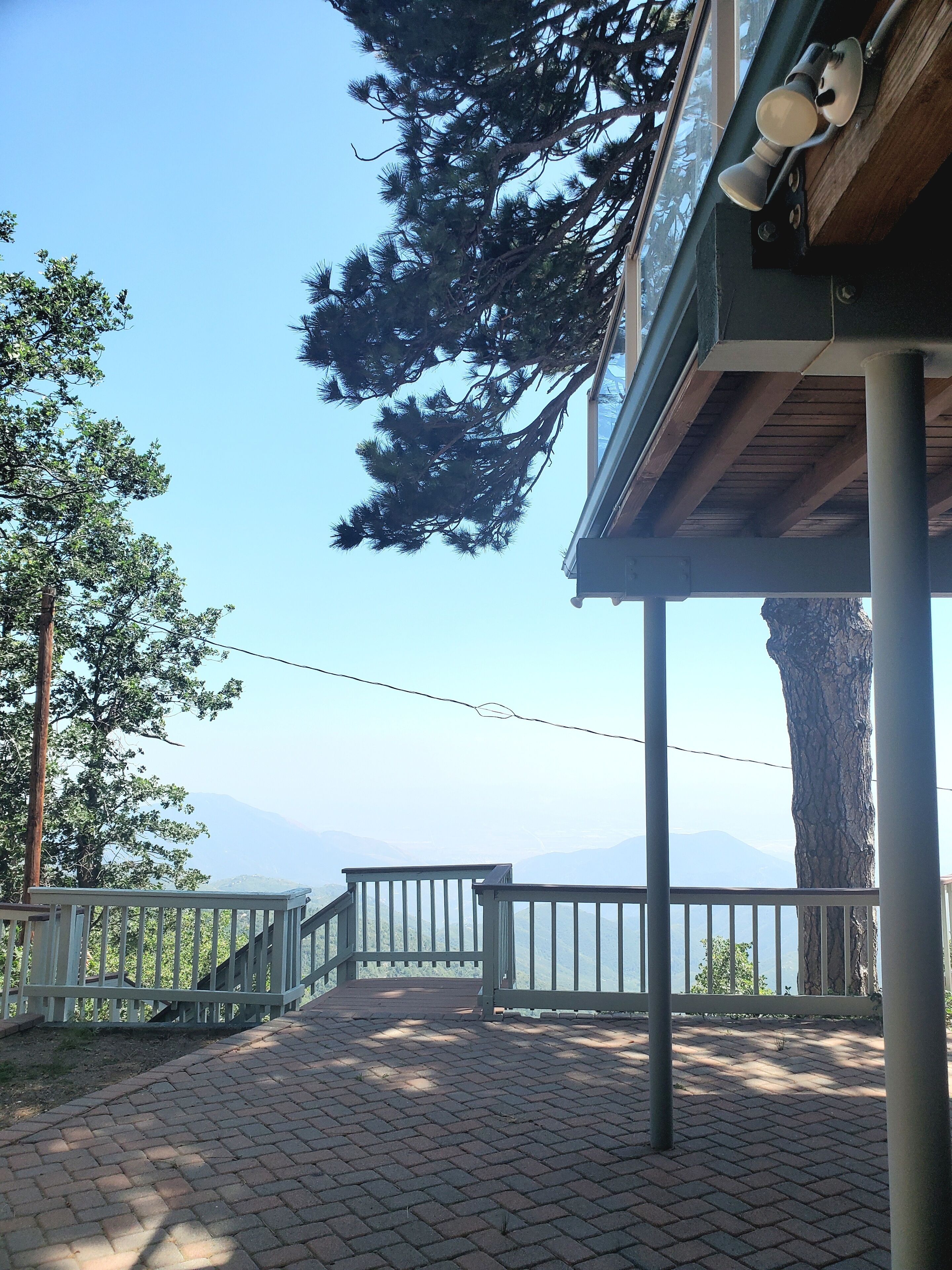 A covered outdoor area with a wooden deck, metal railing, and a view of distant mountains.