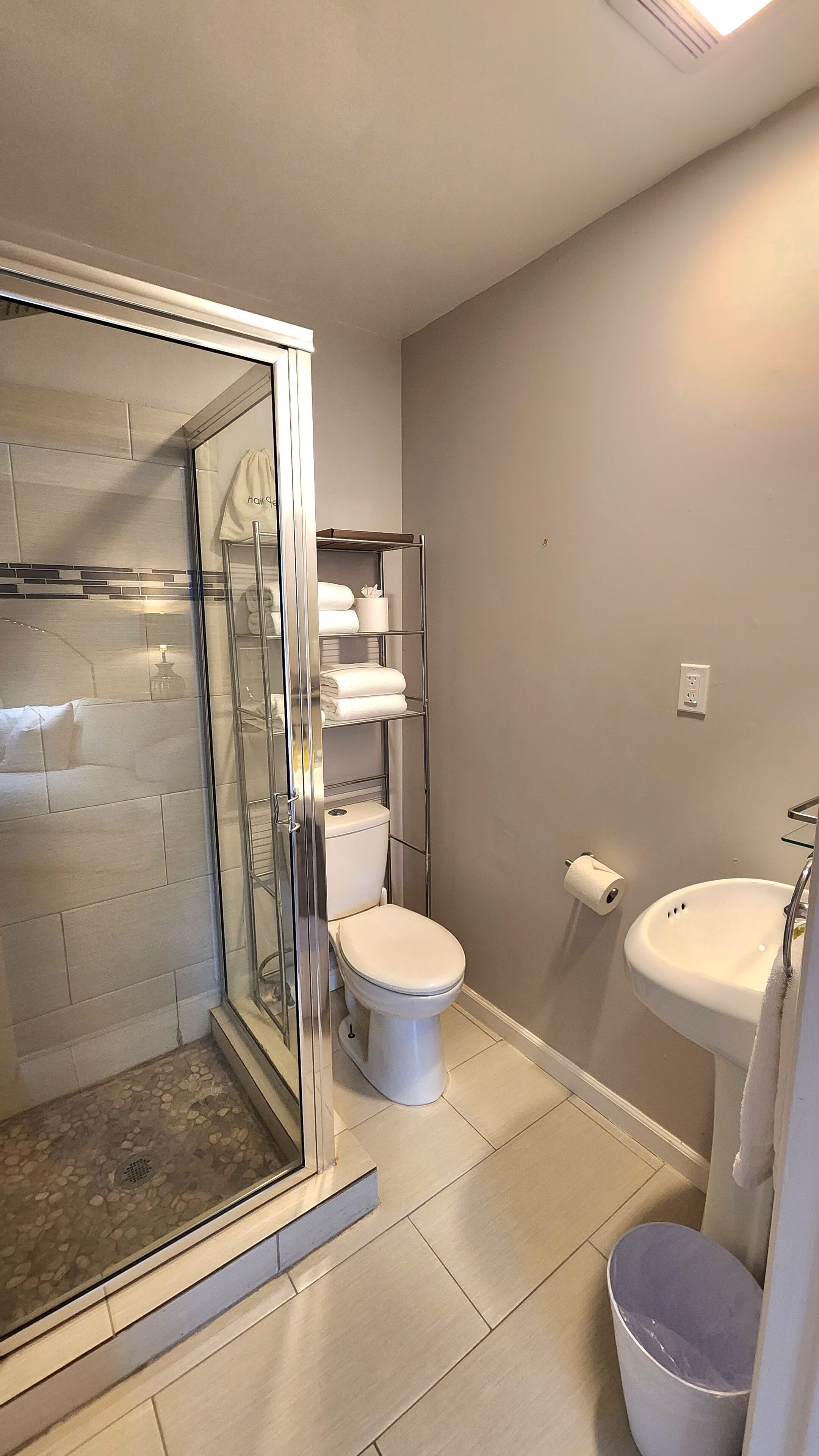 Un baño con ducha envuelta en vidrio, inodoro, lavabo y toallero.