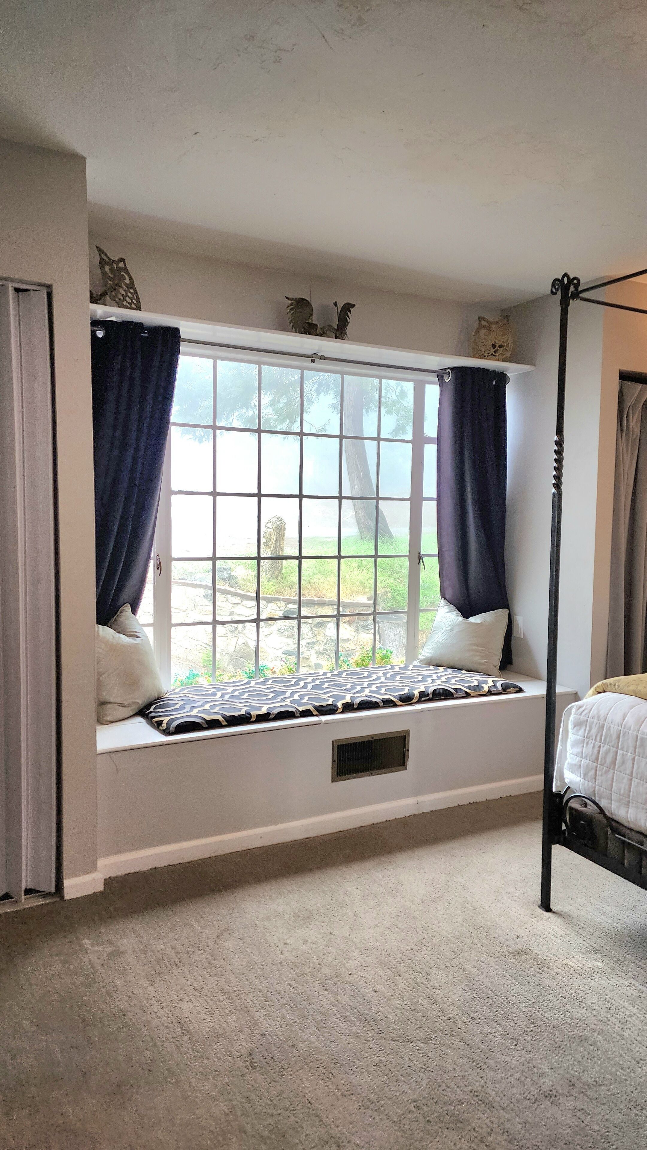Un dormitorio con un asiento junto a la ventana, una cama y un dosel.