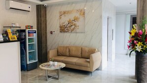 A modern lobby with a beige sofa, a small round table with magazines, a refrigerator, and a large floral artwork on the wall. - Rublin Hotel (Cebu City)