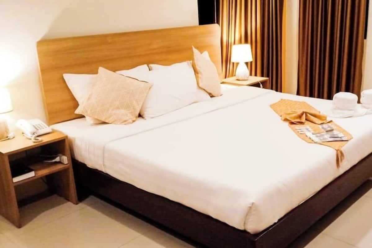 A hotel room with a large bed, wooden headboard, bedside tables with lamps, and a neatly made bed with a folded towel and a magazine.