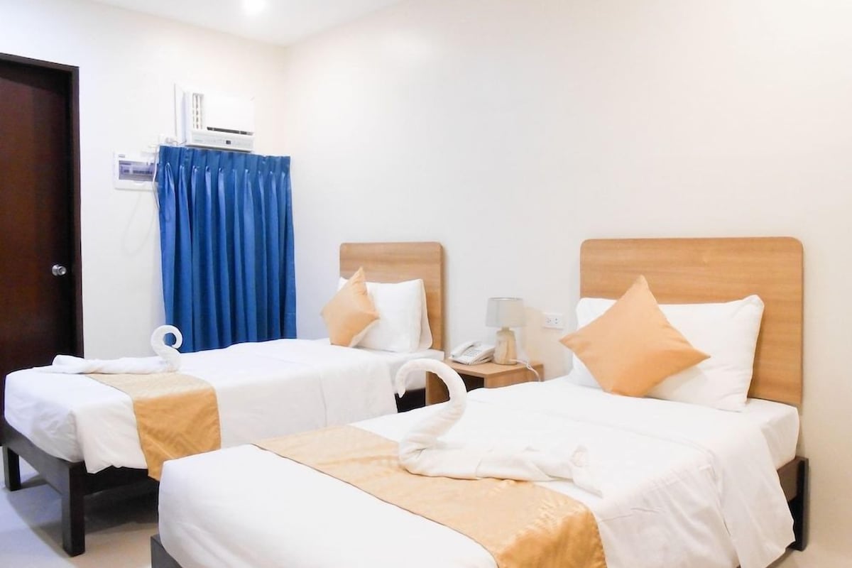 Habitación de hotel con dos camas, una mesita de noche con lámpara, un teléfono y una cortina.